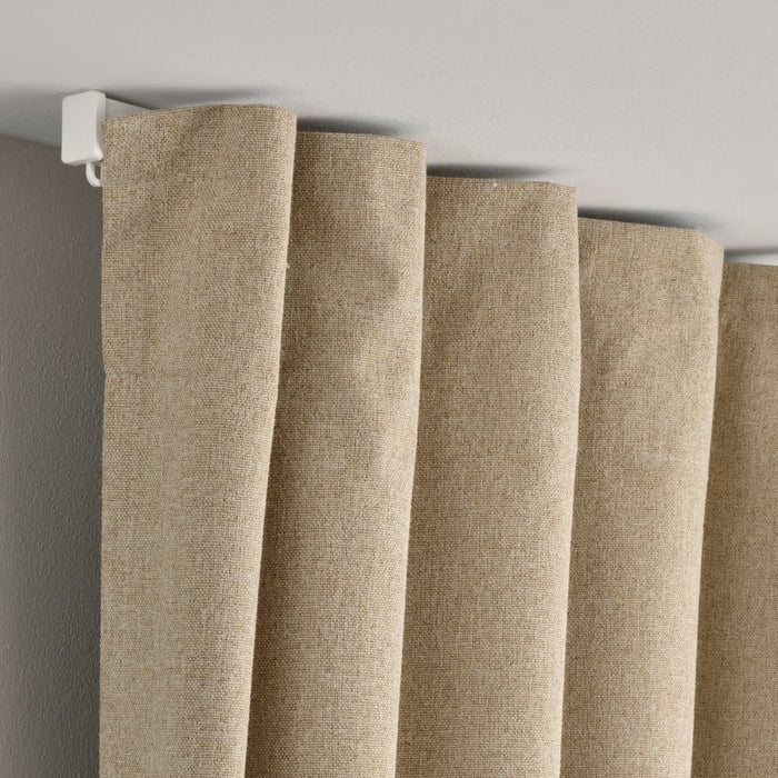 Close-up of beige curtains hanging on a rod against a gray wall.