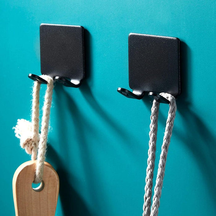 Two black metal wall hooks on teal wall holding rope and wooden-handled item