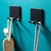 Two black metal wall hooks on teal wall holding rope and wooden-handled item
