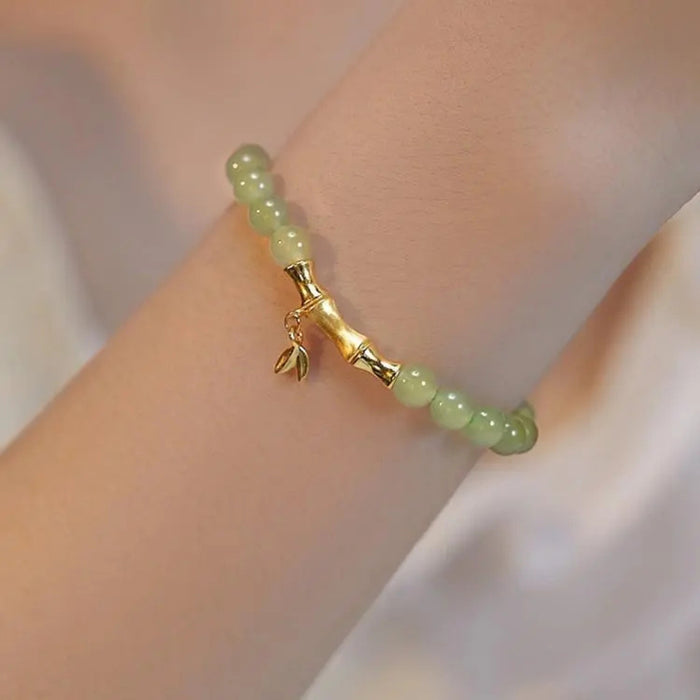 Green beaded bracelet with gold clasp on a wrist against a neutral background