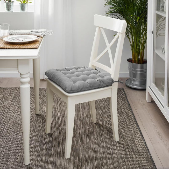 White chair with a gray cushion on a wooden floor in a room with a table and plants.