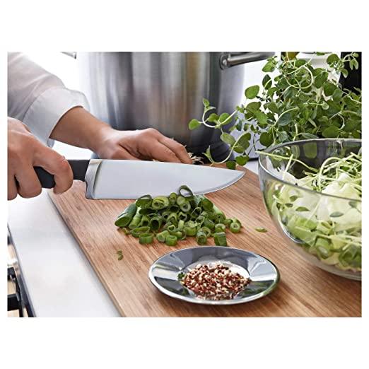 Person chopping green onions on a wooden cutting board with a knife, surrounded by kitchen items.