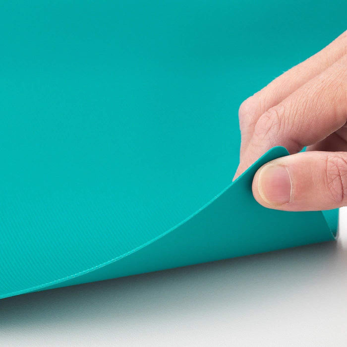 Hand holding a turquoise sheet of paper against a teal background