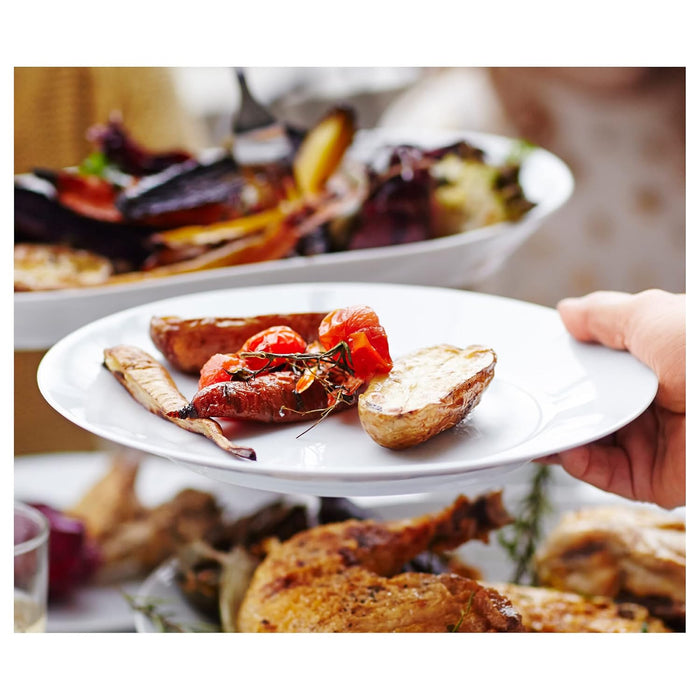 Plate of roasted vegetables and potatoes with a blurred background of more food.