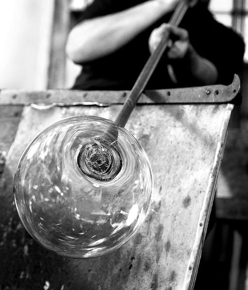 Glassblowing process with a glass object being shaped by a tool.