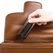 Person using a leather brush on a brown leather bag