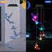 Butterfly-themed solar-powered LED wind chime decoration shown in a side-by-side comparison. Daytime view displays translucent blue butterflies hanging from strings, while nighttime view showcases glowing butterflies in vibrant colors, creating a dazzling garden display.