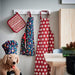 Patterned aprons and pot holders hanging on a wall with a dog wearing a chef's hat in the foreground.
