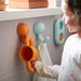 Child-friendly bathroom setup featuring HUMLESJÖN hook in orange/turquoise beside playful accessories and storage bins.

