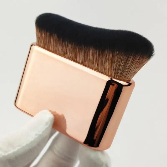 gold rectangular makeup brush with gradient bristles presented in hand photography