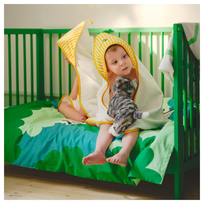 Baby in a yellow and white hooded towel sitting on a green crib with a gray cat.