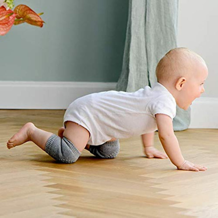 Baby anti-slip knee pads – baby crawling on wooden floor in white onesie and grey pads, plant in background