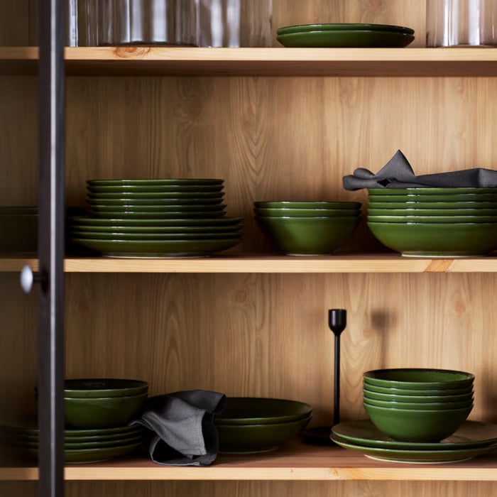 IKEA PELARKAKTUS green plates and bowls neatly stacked and organized on a wooden kitchen cabinet shelf.
