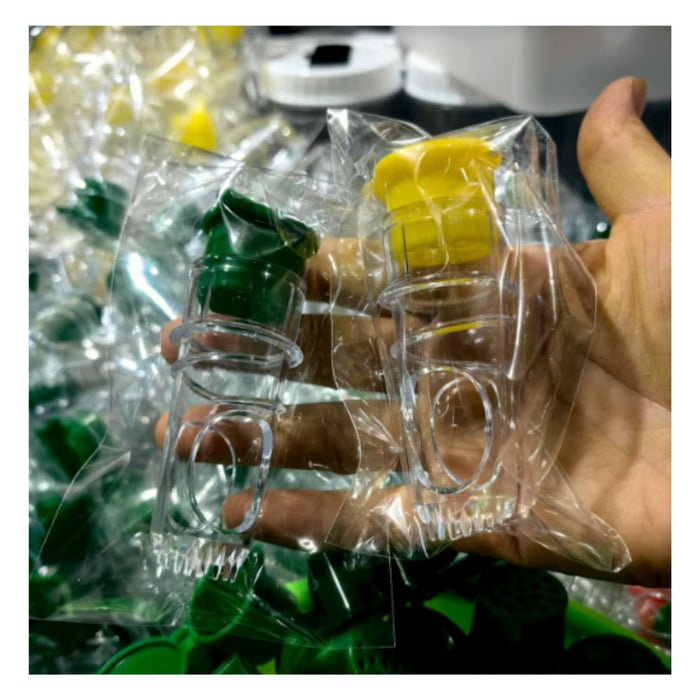 A hand holding two small clear plastic bottles with flip-top dispensers, one green and one yellow, wrapped in clear plastic packaging.