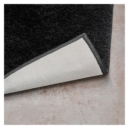 Close-up of a black rug with a textured white border on a concrete floor.