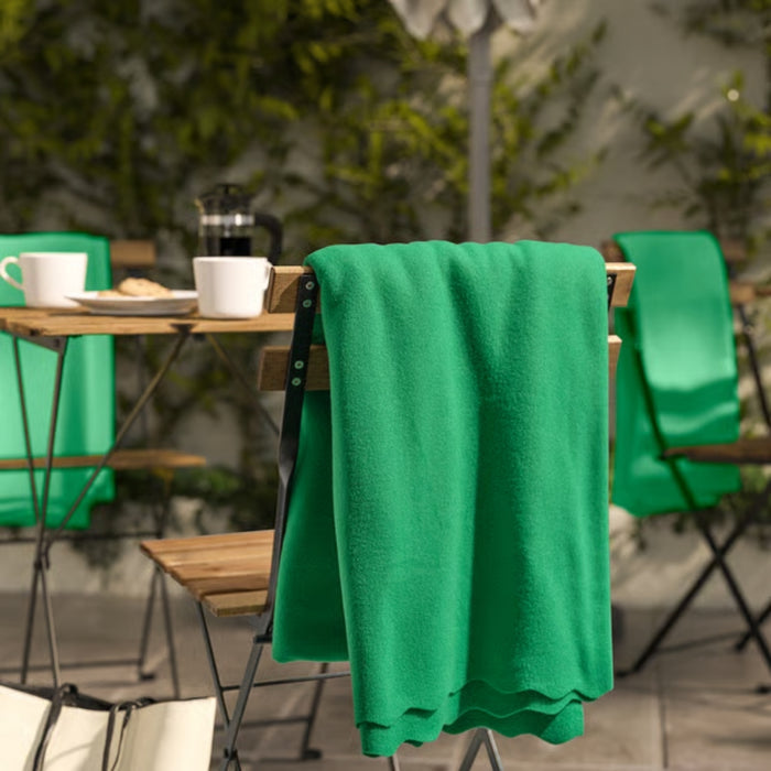 DAGGKÅPOR throw, green, 130x170 cm. Draped over outdoor chair in garden setting with coffee mugs and French press on table – adds cosy charm to patio mornings – 90602695.