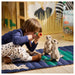 Child sitting on cheetah mat with toy monocular, playing with meerkat plush toys in wildlife-themed room