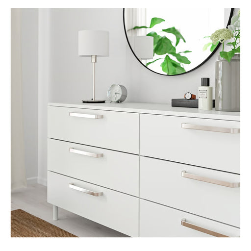 White dresser with silver handles in a room setting.