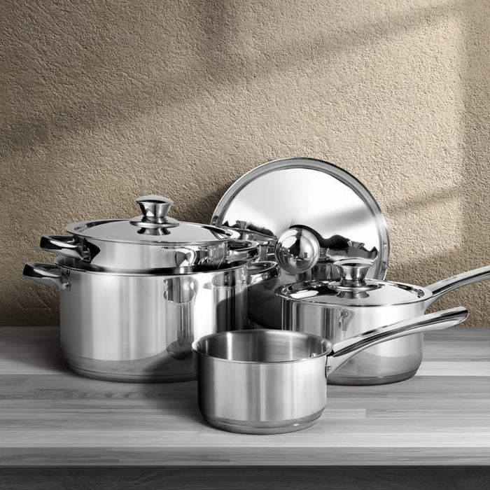Set of stainless steel cookware on a wooden surface with a beige wall background