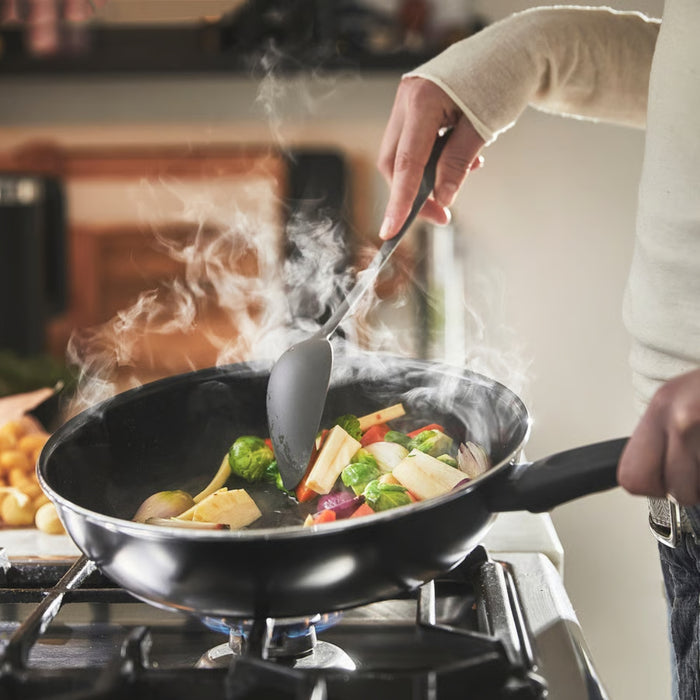 Person cooking vegetables in a pan with steam rising