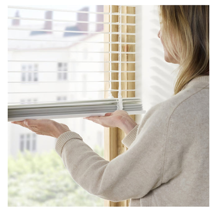 Person adjusting window blinds with a blurred indoor background