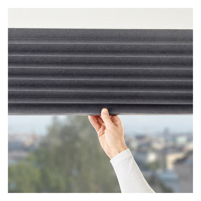 Person holding up a gray pleated blind with a blurred outdoor background