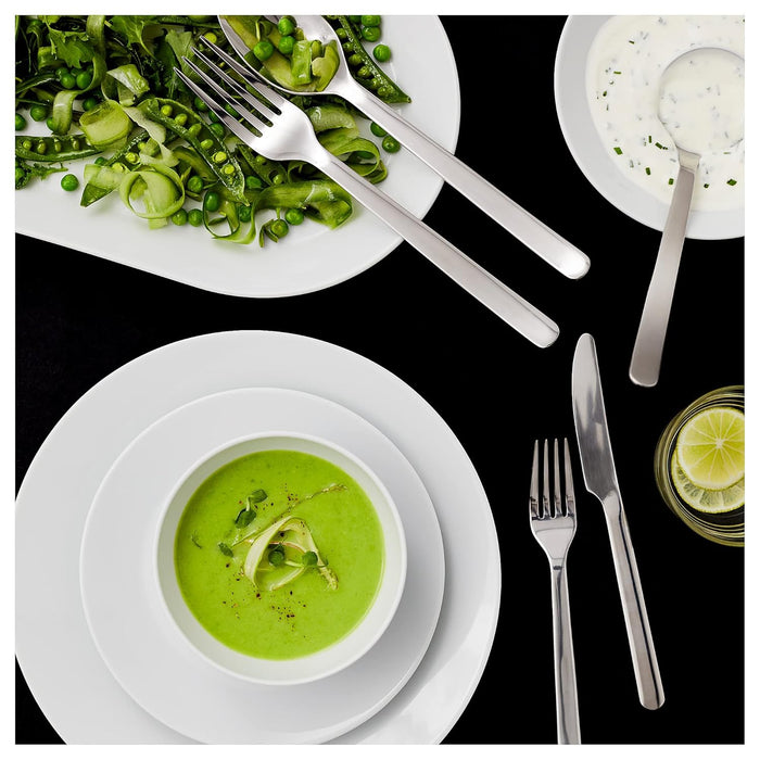 Green soup in a bowl with a side salad and cutlery on a black background