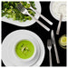 Green soup in a bowl with a side salad and cutlery on a black background