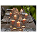 Dining table set with candles and glasses, surrounded by greenery