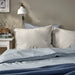 BERGPALM pillowcase, grey/striped, 50x80 cm. Shown on bed with matching striped bedding, white nightstand, books, and wall lamp – adds calm, lived-in charm to bedroom – 80577149.