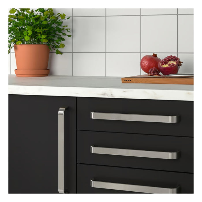 Black kitchen cabinet with silver handles on a white countertop, featuring a potted plant and fruits.