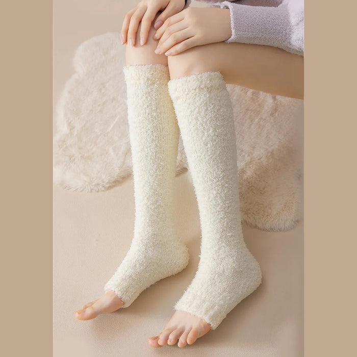 Person seated on beige surface wearing cream fuzzy leg warmers from knee to ankle - 