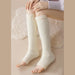 Person seated on beige surface wearing cream fuzzy leg warmers from knee to ankle - 