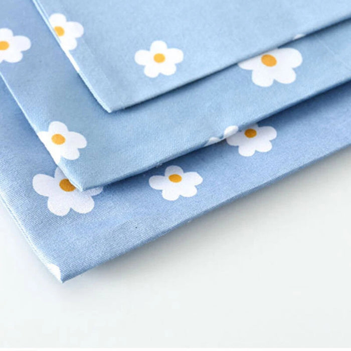 Stacked pieces of light blue fabric with white and yellow floral pattern – 1598445710448 14078092