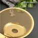 Golden stainless steel fine mesh strainer with a circular design and central drainage hole, set against a dark background. The utensil is labeled “STAINLESS STEEL KITCHEN UTENSILS – Fine oil draining net efficiently filters excess oil residue,” highlighting its precision mesh structure for oil separation. Accompanied by green leaves and a grey cloth, the image evokes an elegant and efficient kitchen environment -1600003112383 13034147.
