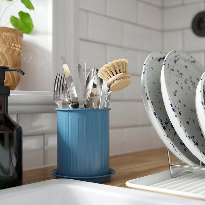 Blue utensil holder with cutlery and a dish brush on a kitchen counter.