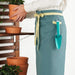Person holding a potted plant with a teal apron featuring a tool pocket.