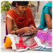 Woman sitting on the floor working on a piece of fabric with another person partially visible.