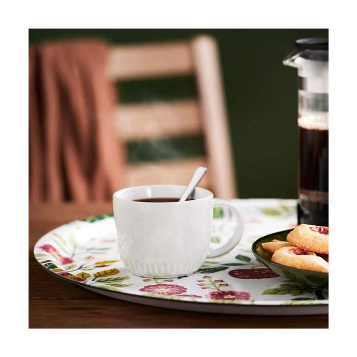 White mug with coffee on a floral plate with cookies and a jar of jam.