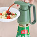 Green bottle with a nozzle being used to pour sauce over a dish of food.
