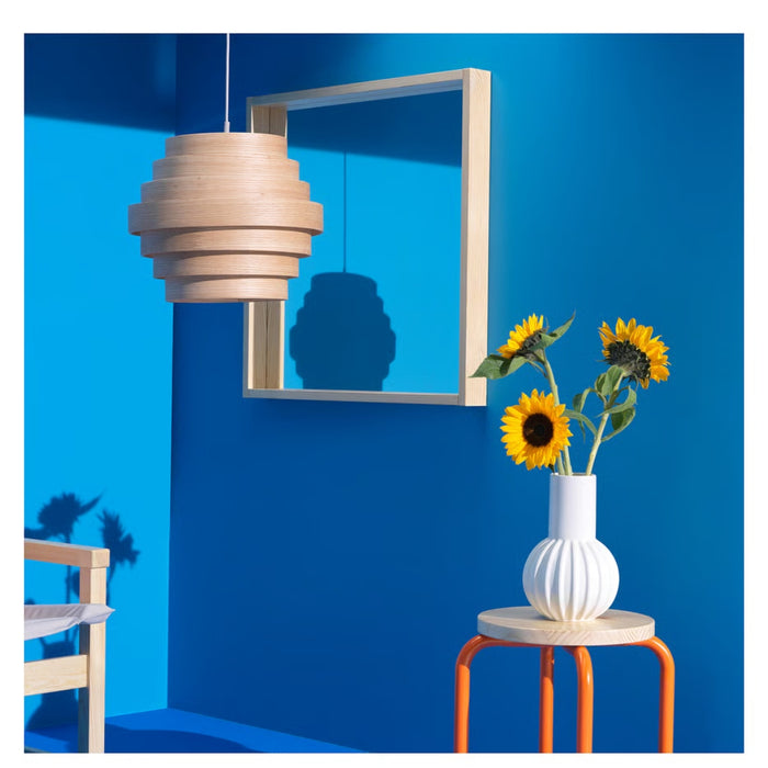 Modern interior with a blue wall, wooden pendant lamp, mirror, and vase with sunflowers.