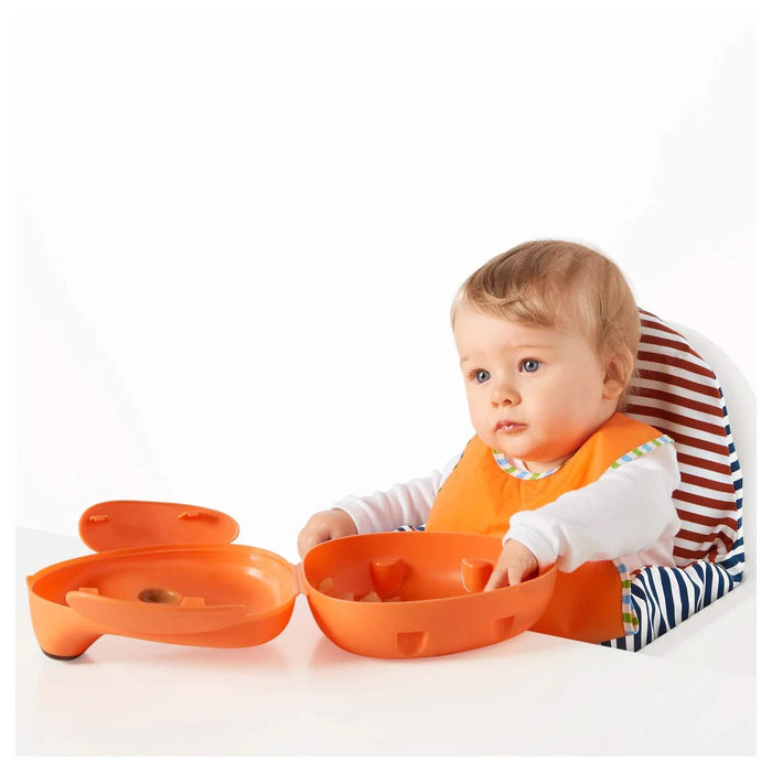 Baby wearing an orange bib sitting in a high chair with a white background