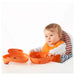 Baby wearing an orange bib sitting in a high chair with a white background