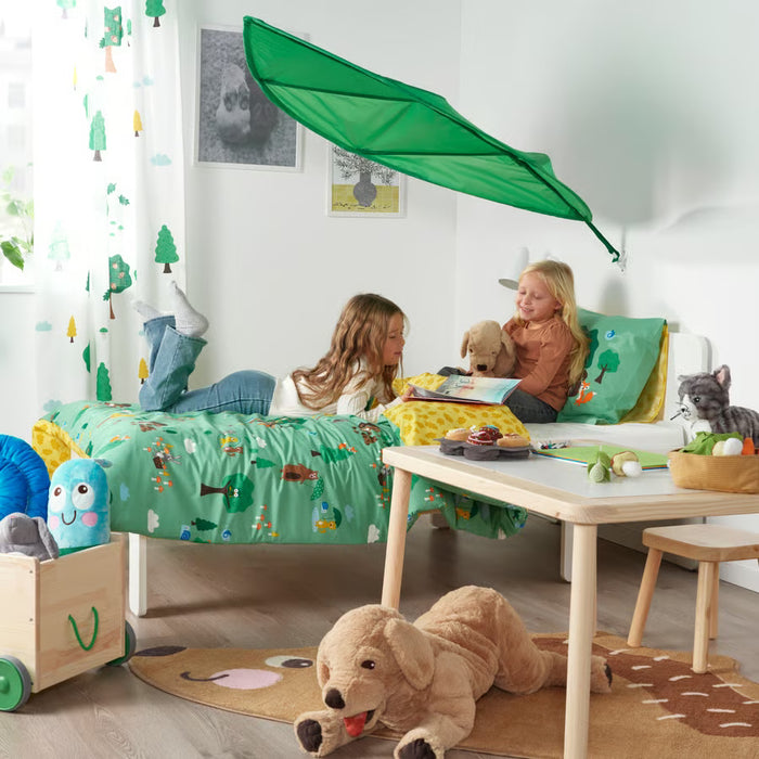Two kids playing on a bed under the green LÖVA leaf canopy with toys around