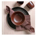 Brown ceramic bowl on a black plate with a folded brown napkin on a striped tablecloth.