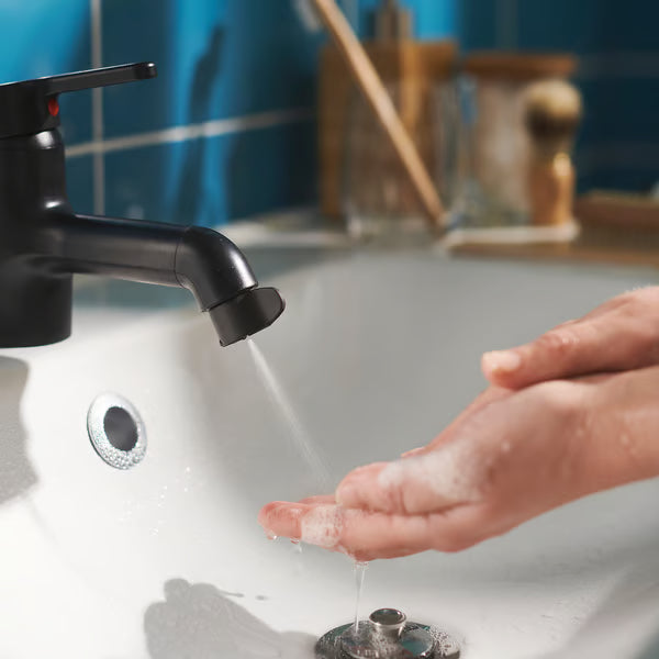 Person washing hands under black mixer tap with ÅBÄCKEN nozzle blue tiled wall backdrop