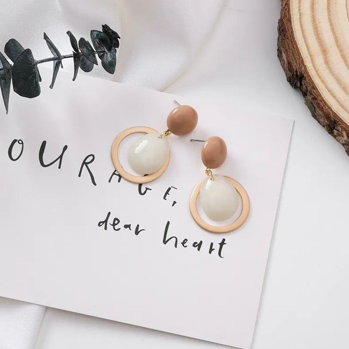 Pair of earrings with wooden and beige circular designs on a white surface with text.