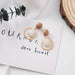 Pair of earrings with wooden and beige circular designs on a white surface with text.