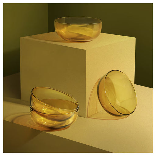 Three IKEA AROMATISK yellow glass bowls displayed on beige stand and table surface