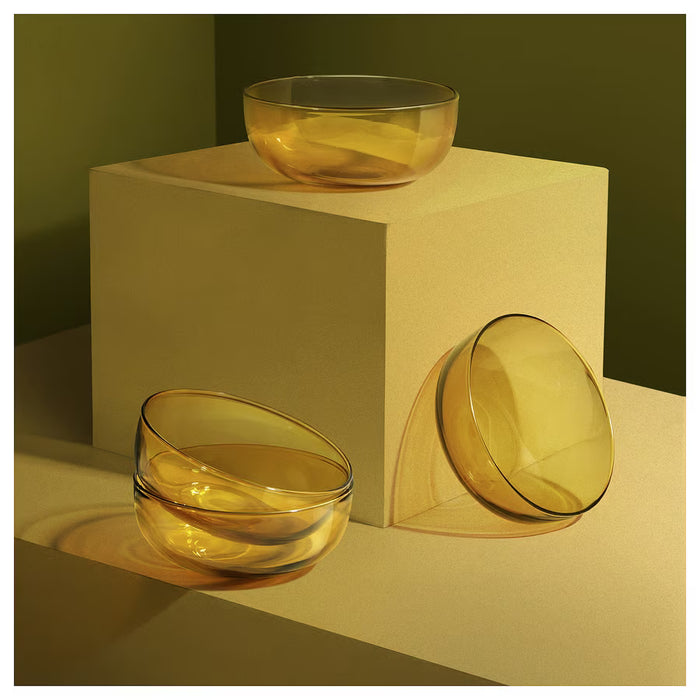 Three IKEA AROMATISK yellow glass bowls displayed on beige stand and table surface